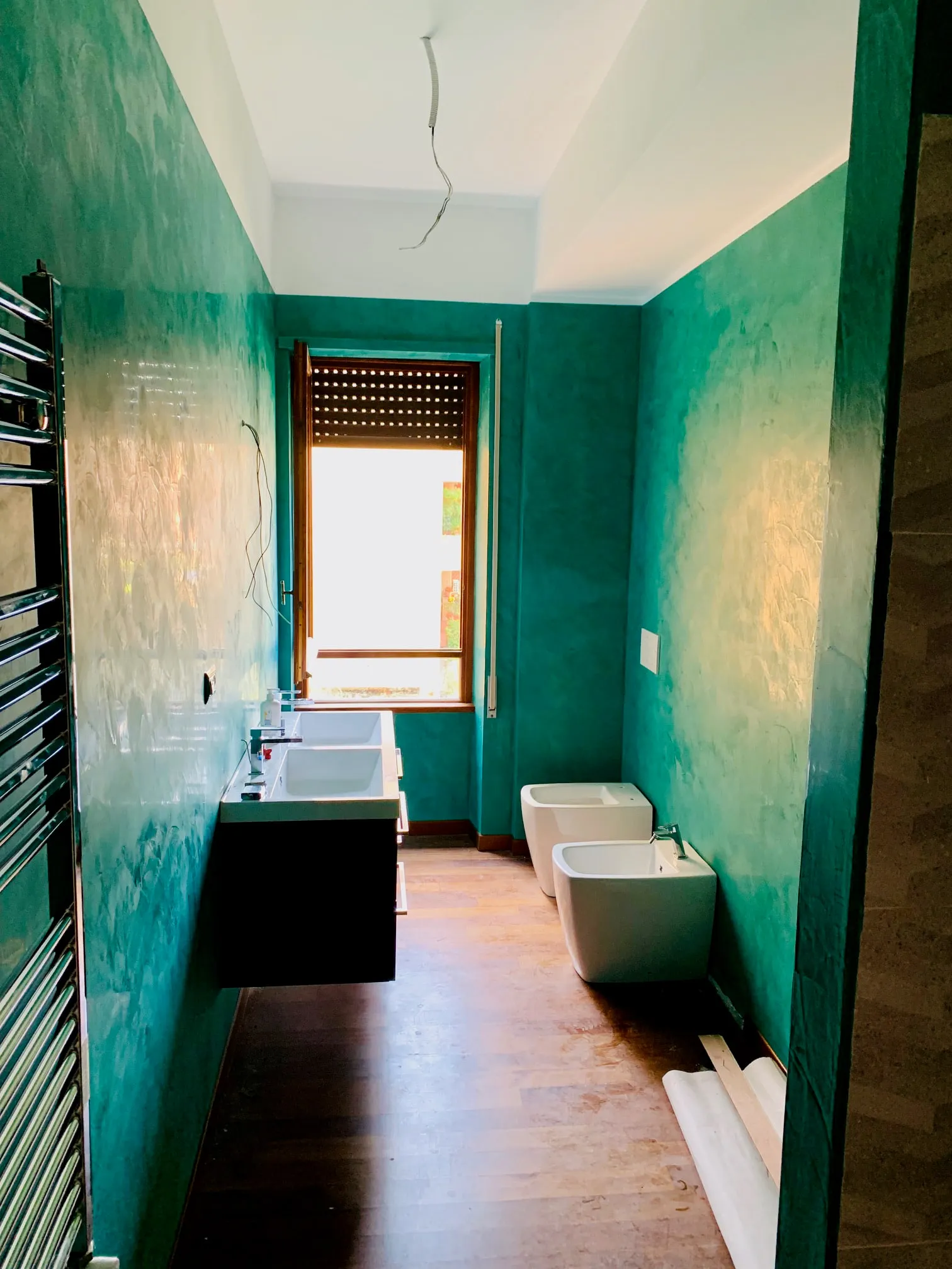 Bagno con pareti spatolate verde smeraldo, doppio lavabo su mobile sospeso scuro e sanitari bianchi