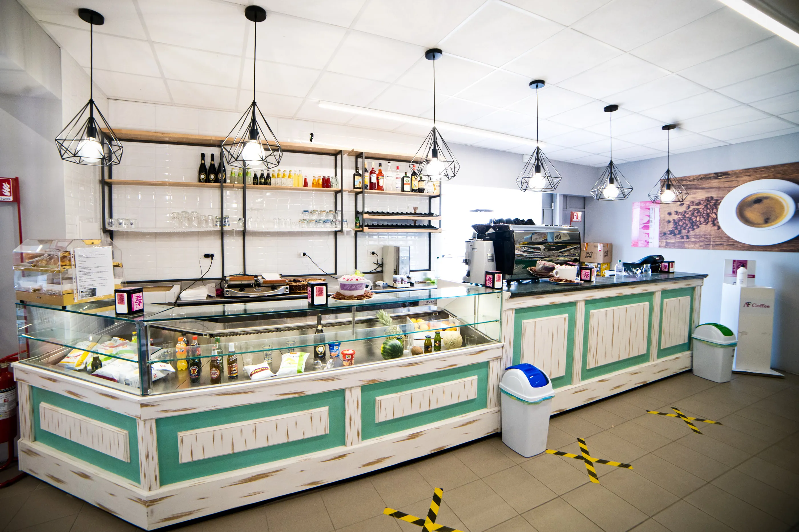 Banco bar e gastronomia con vetrine refrigerate, scaffalature in legno e lampade a gabbia sospese