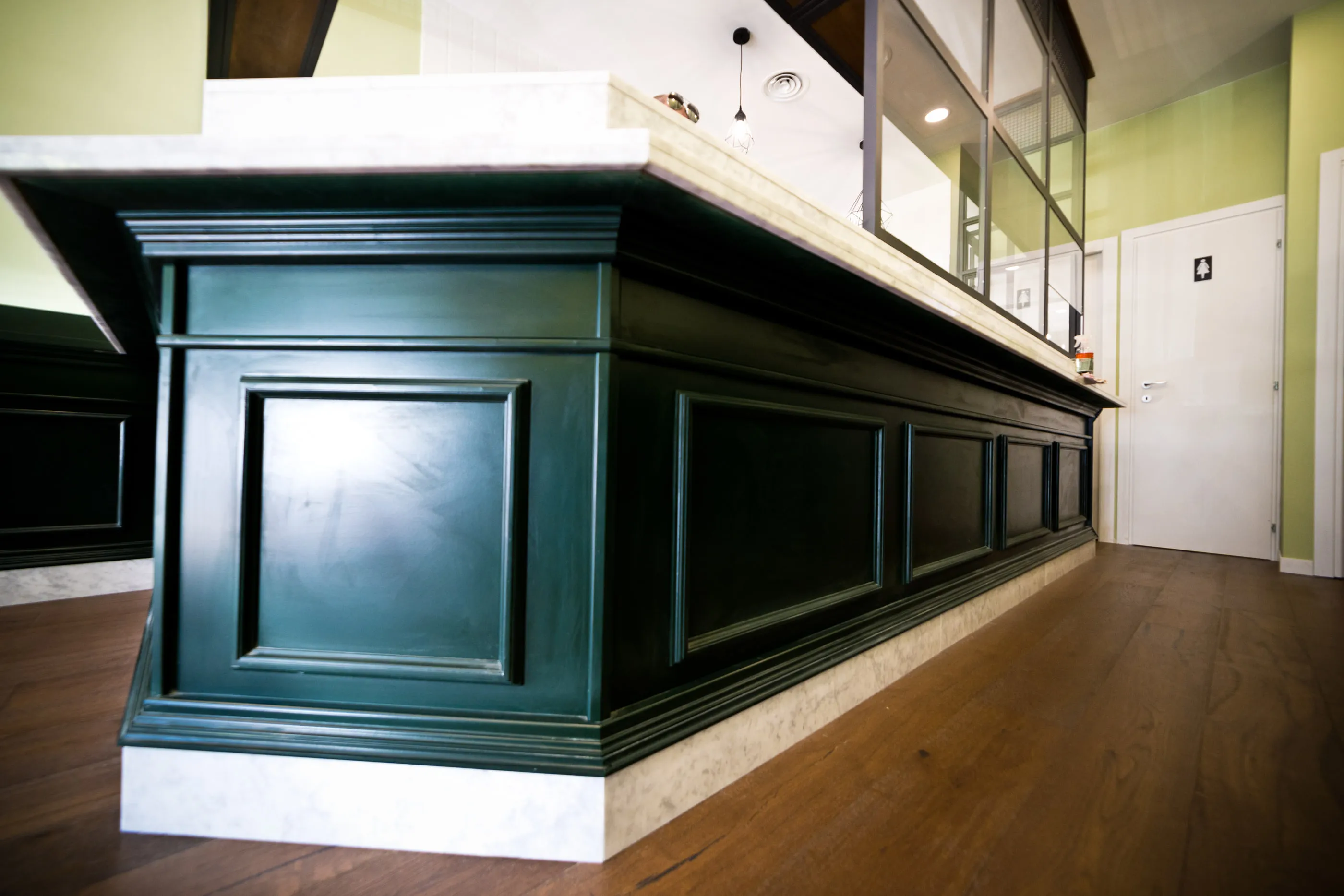 Dettaglio del fianco di un banco bar in legno laccato verde scuro, con top e zoccolo in marmo bianco
