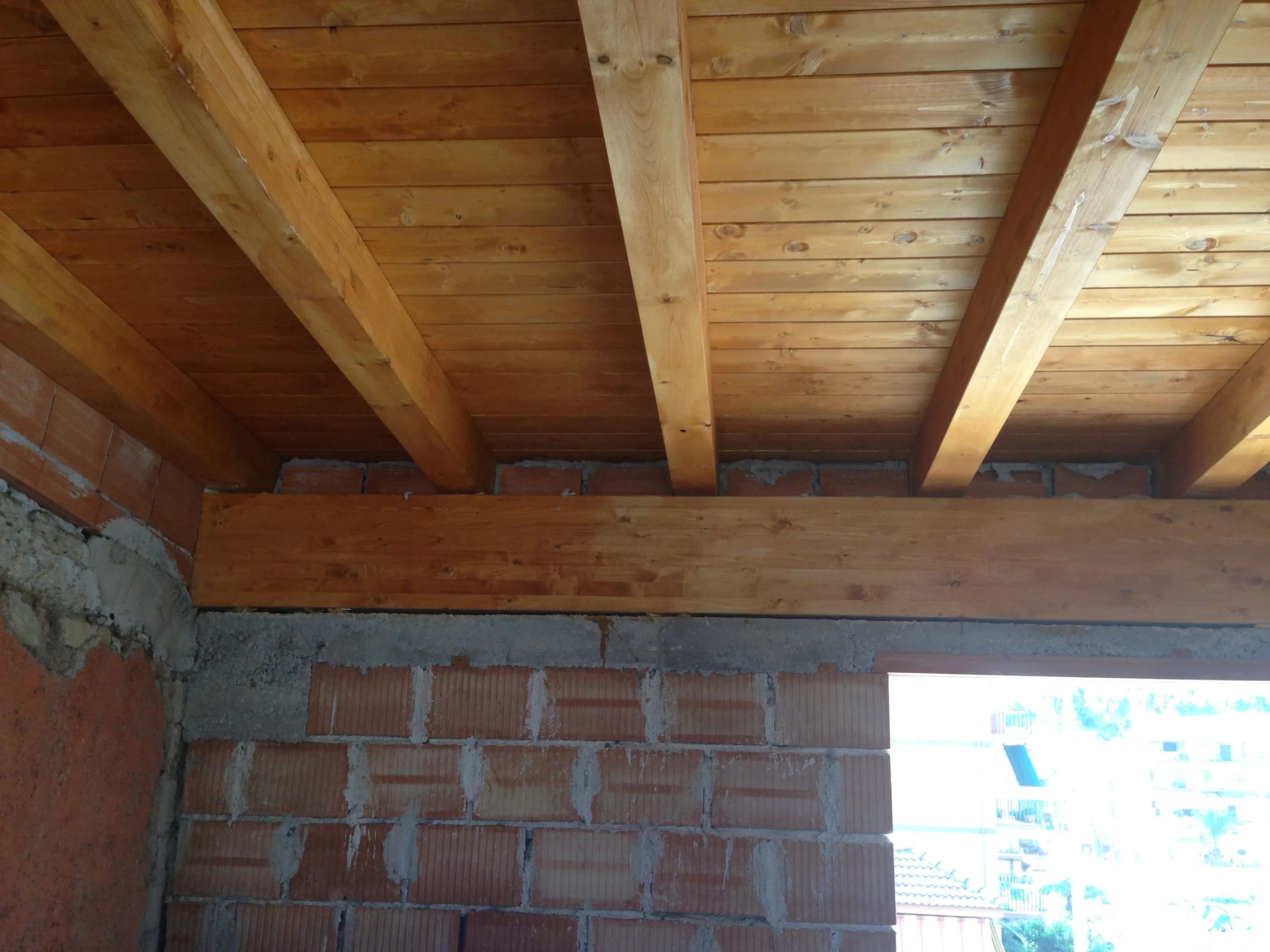 Copertura in legno con travi e tavolato a vista appoggiata su muratura in laterizio, vista dal basso