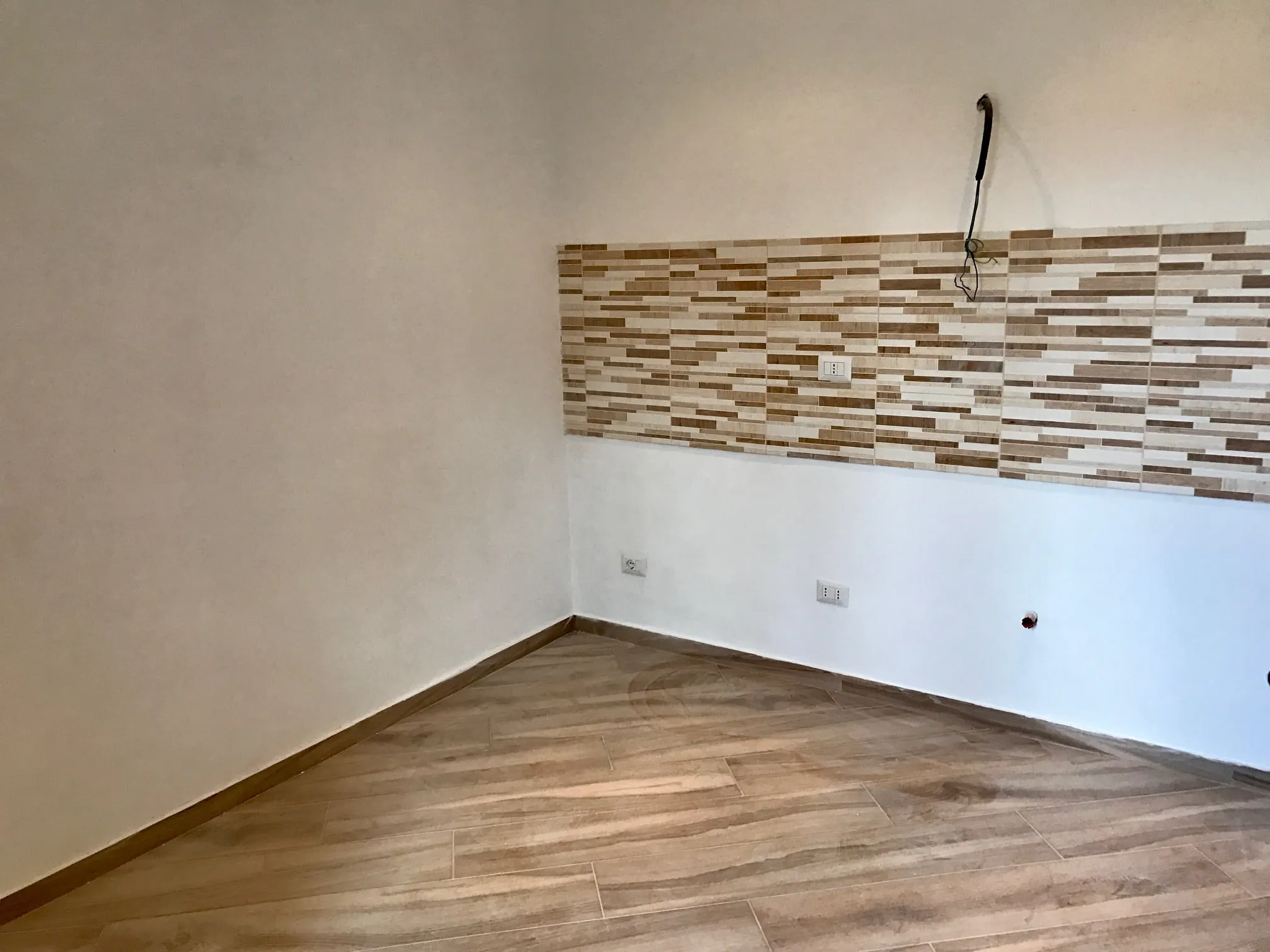 Parete con fascia orizzontale rivestita in listelli di legno di tonalità diverse, sopra un pavimento in gres effetto rovere