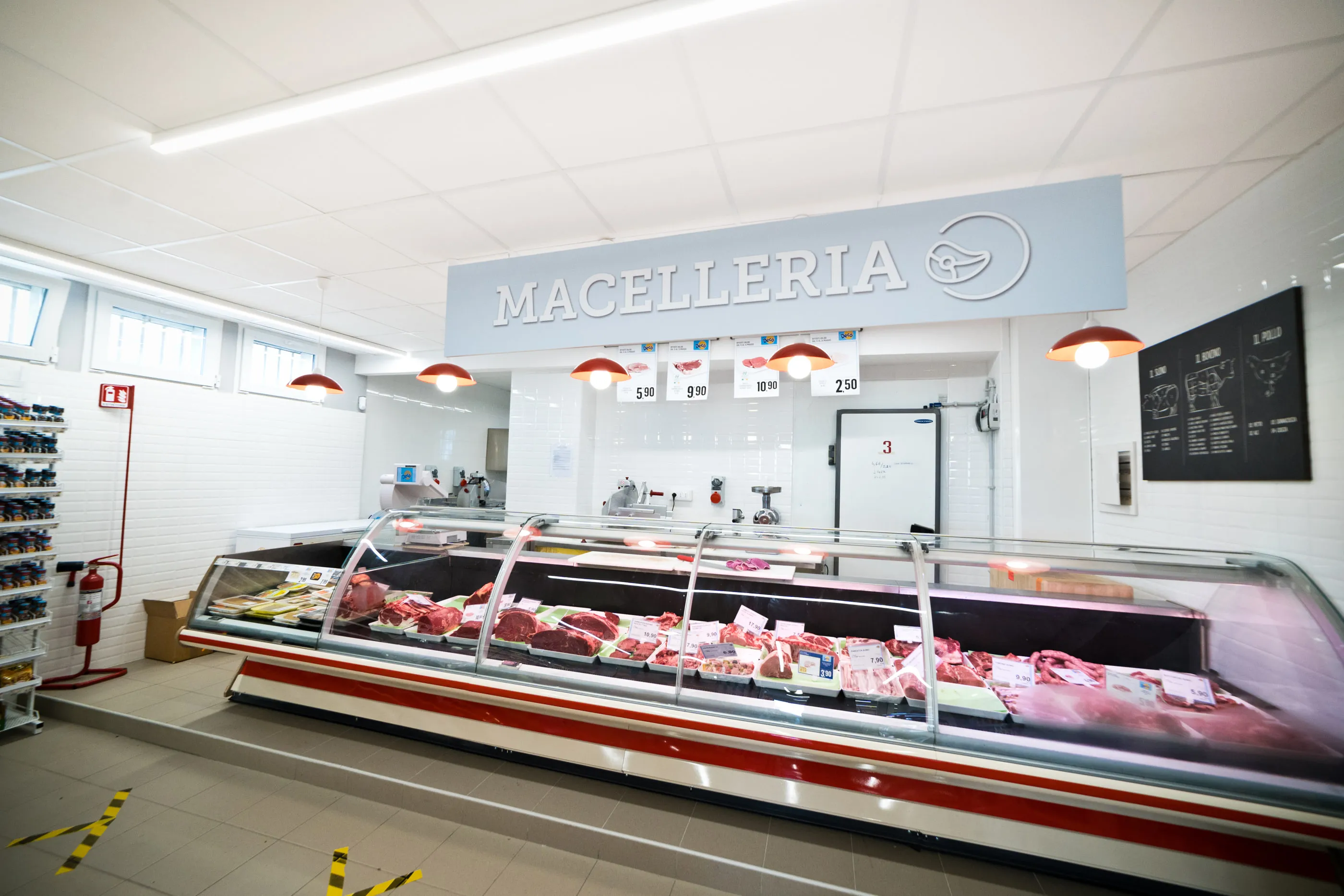 Reparto macelleria di un supermercato con banco refrigerato, insegna sospesa e controsoffitto illuminato